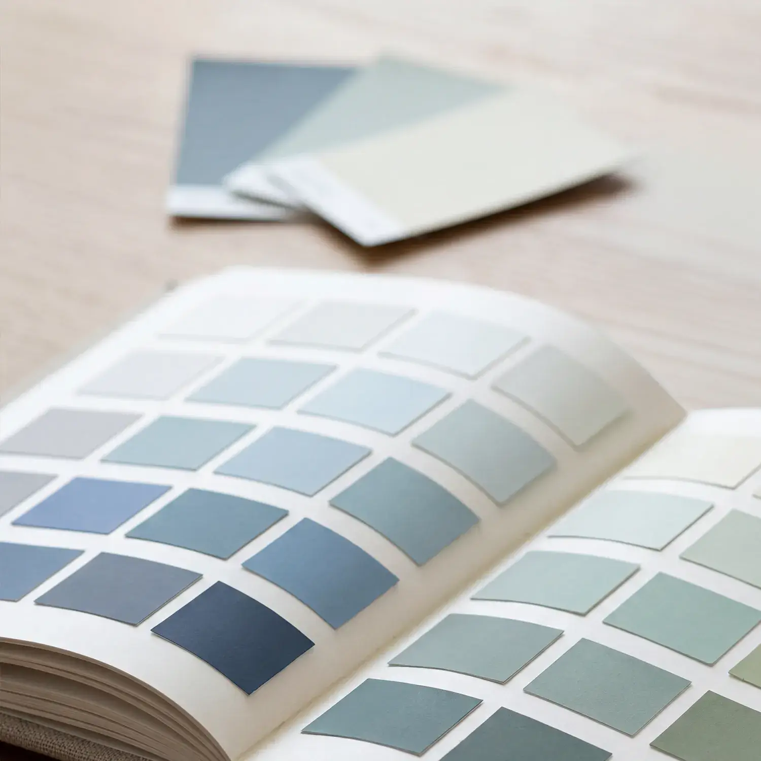 Aufgeschlagenes Farbfächerbuch mit verschiedenen Blau- und Grautönen, das zur Auswahl harmonischer Wandfarben bei der Idee & Planung vom Malerbetrieb in Düsseldorf durch Malermeister Kleinau genutzt wird