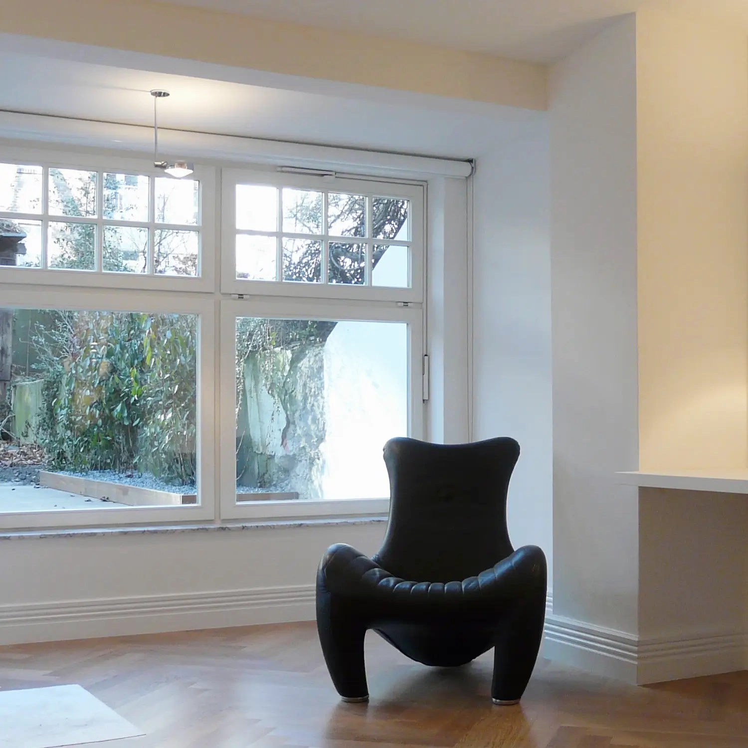 Heller Wohnraum mit großem Fenster, weiß gestrichenen Wänden und modernem Design-Sessel als Beispiel für präzise Innenraumgestaltung durch einen Maler für Anstricharbeiten in Düsseldorf von Malermeister Kleinau